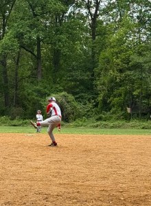 boy in little league uniform in mid-pitch with trees in background
