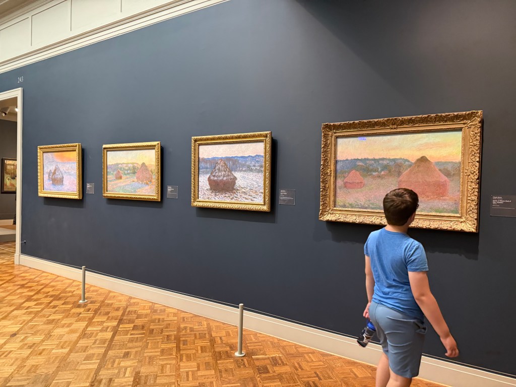 A child looking at a display of four of Monet's haystack paintings in the Art Institute of Chicago